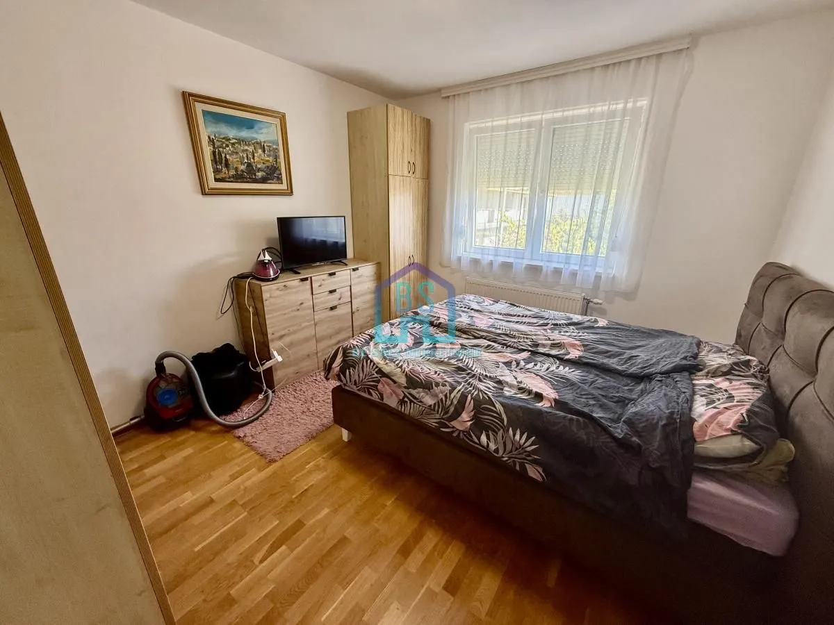 Nameštena spavaća soba sa bračnim krevetom, ormarom i komodom sa televizorom.