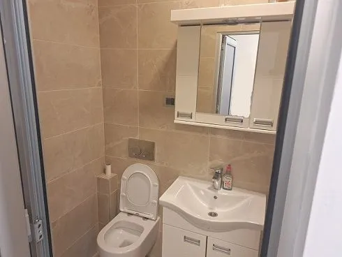 Small bathroom with a sink, cabinet, and toilet lined with beige tiles.