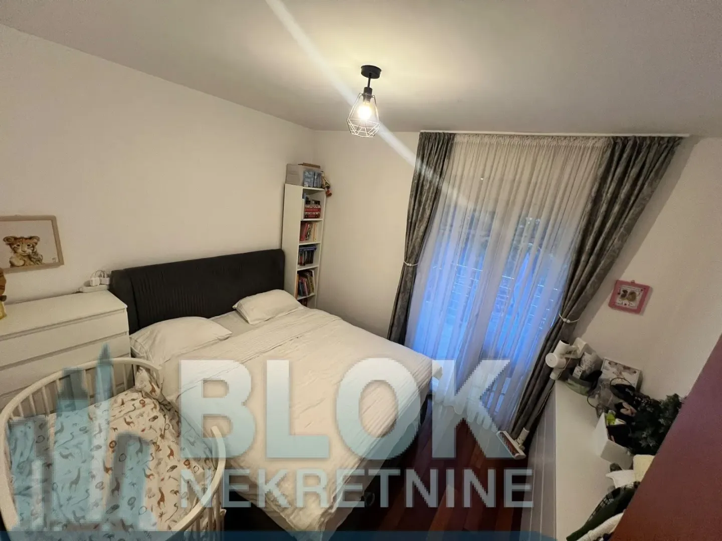 Furnished bedroom with a double bed, a baby crib, and a window with curtains.