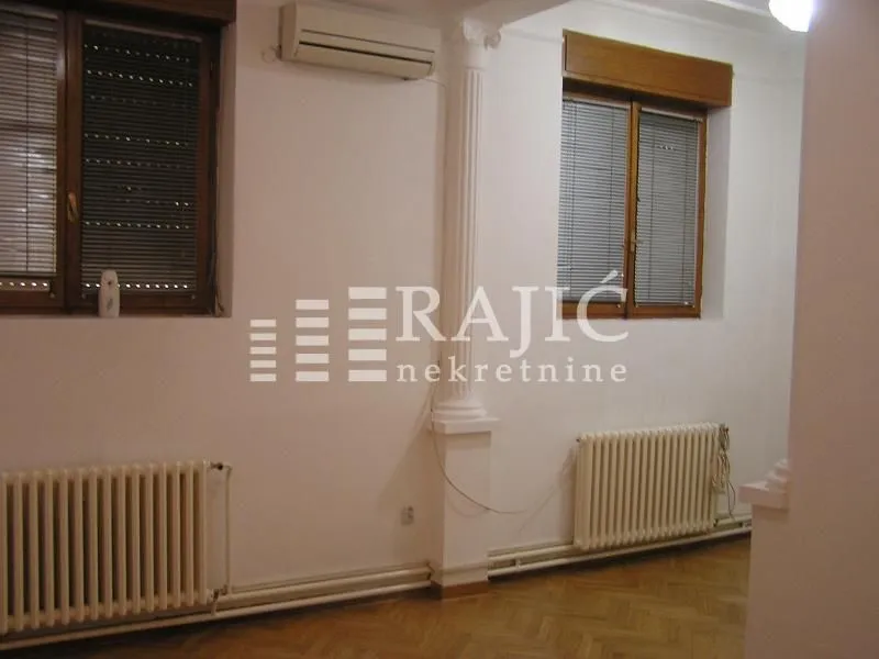 Interior of a room with parquet flooring, windows, and radiators.