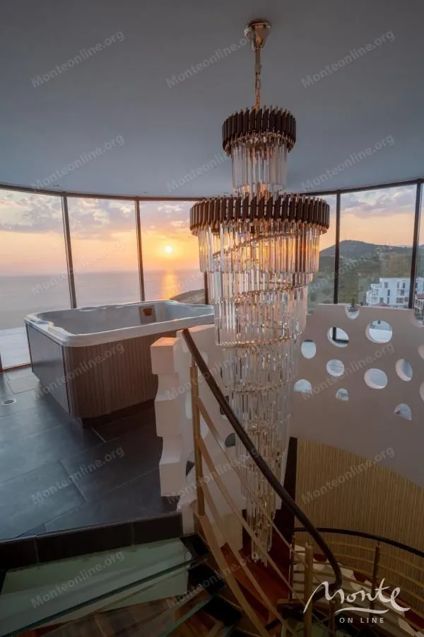 Bathroom with a jacuzzi and sea view next to a staircase with a large chandelier.
