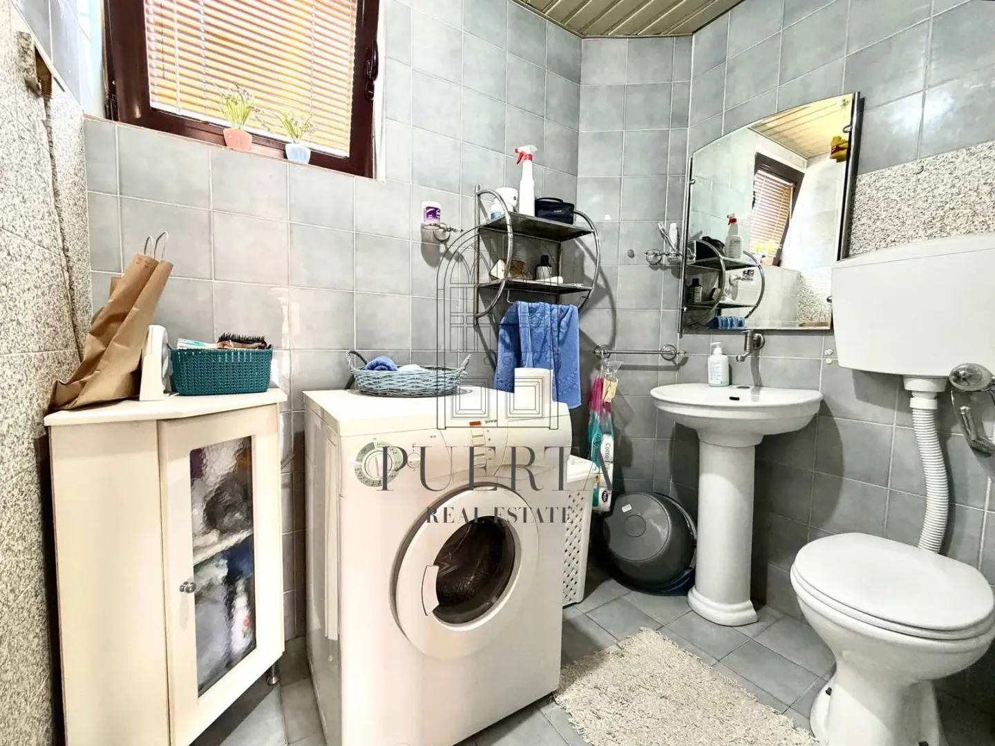 Kupatilo opremljeno sanitarijama, umivaonikom, ogledalom i mašinom za veš.