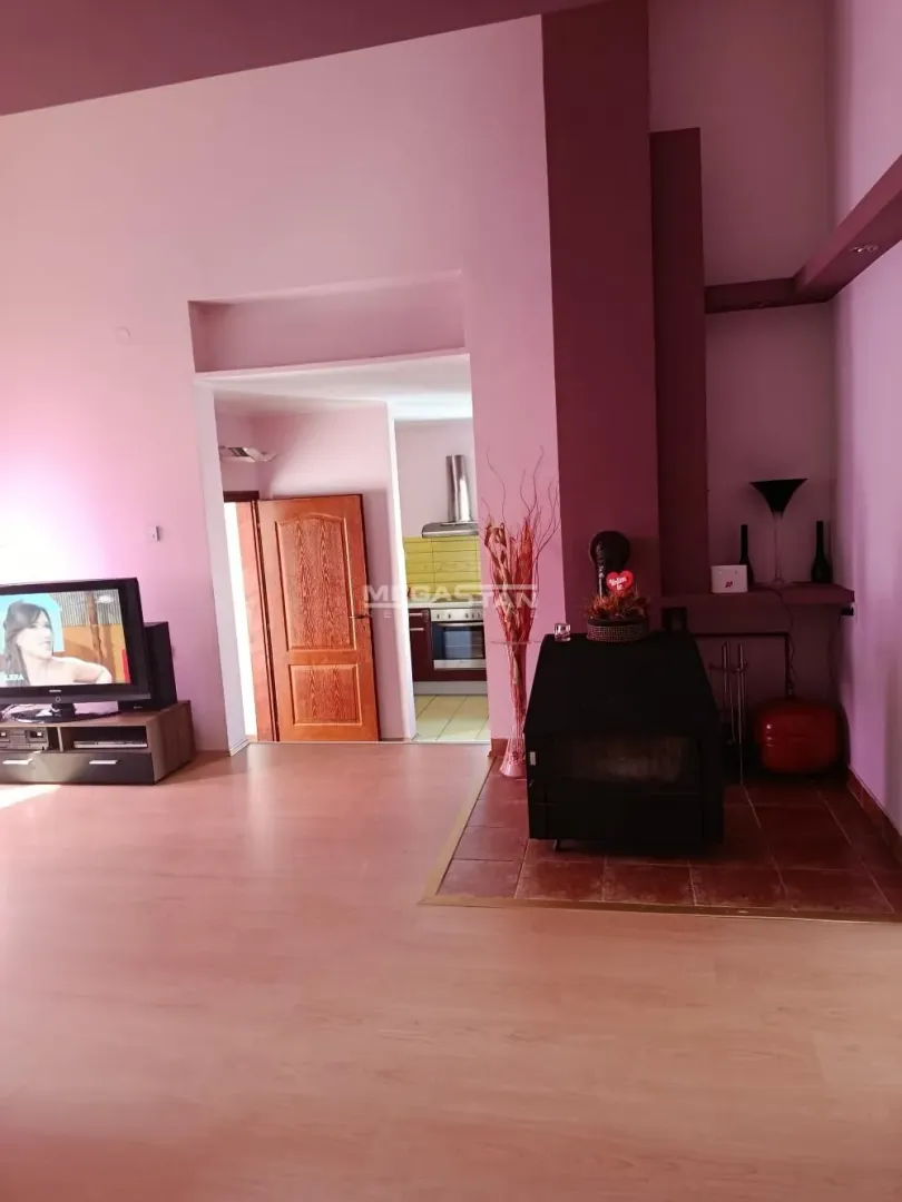 Living room with a fireplace and a view of the kitchen in the background.