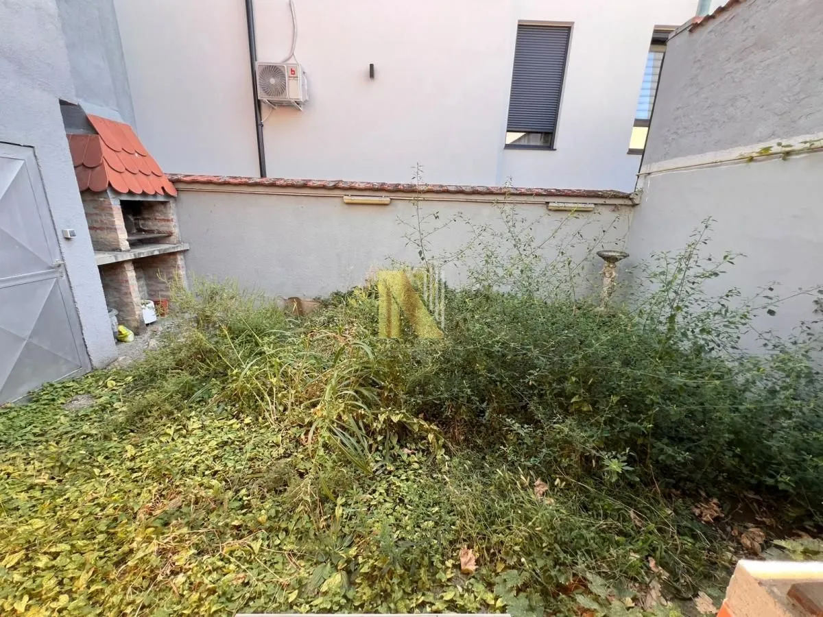 Zaraslo dvorište sa zidanim roštiljem ograđeno zidom.