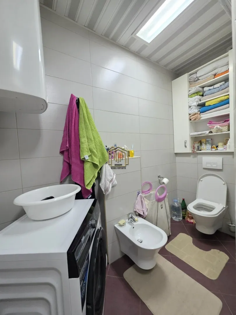 Kupatilo opremljeno sanitarijama, veš mašinom i ugradnim ormarićem za peškire.