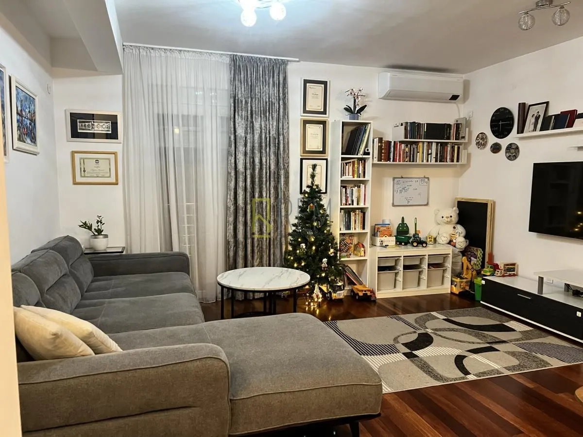 Namještena dnevna soba sa ugaonom garniturom, televizorom i policama za knjige.