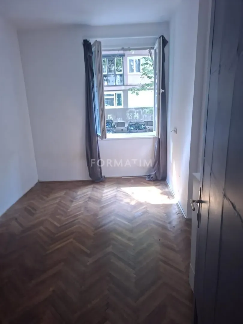 Empty room with wooden parquet flooring and a window overlooking the courtyard.