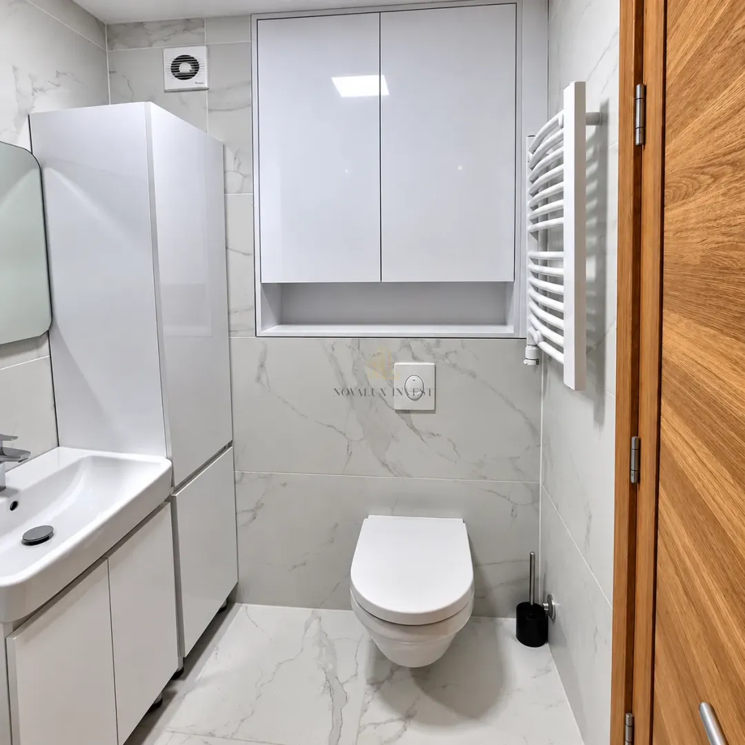 Moderno opremljeno kupatilo sa bijelim sanitarijama i mermernim pločicama.