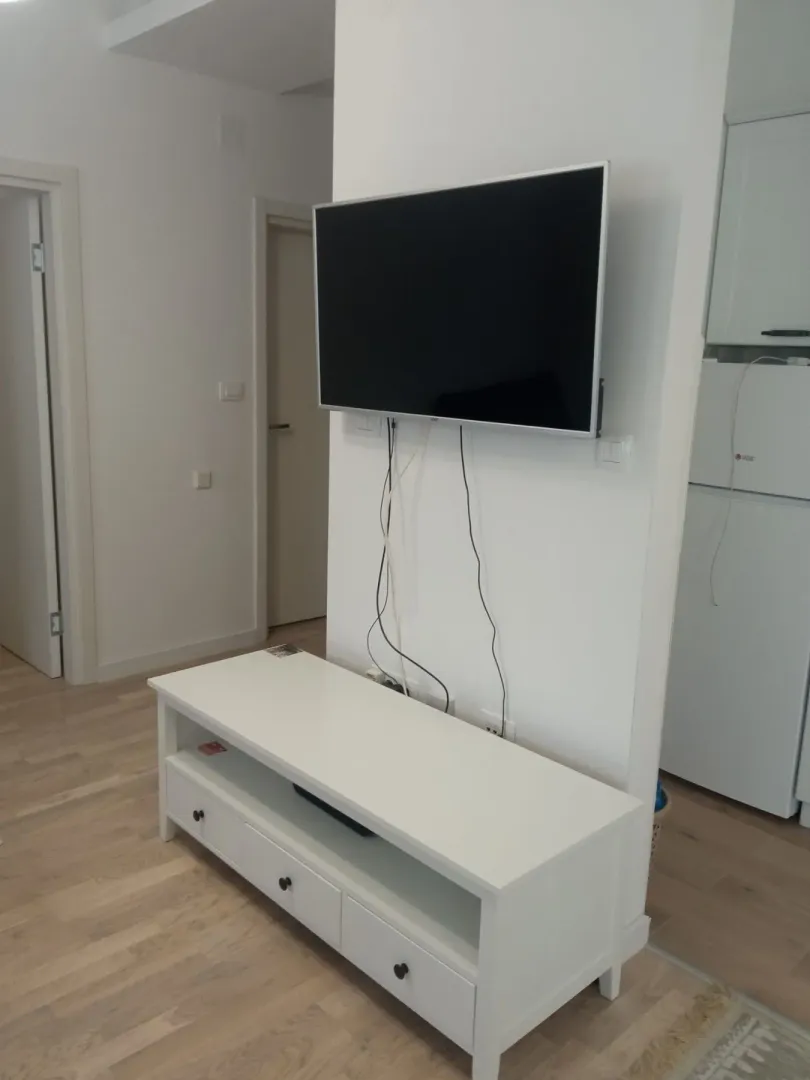 Svijetli dio dnevne sobe sa montiranim televizorom i bijelom komodom ispod njega.