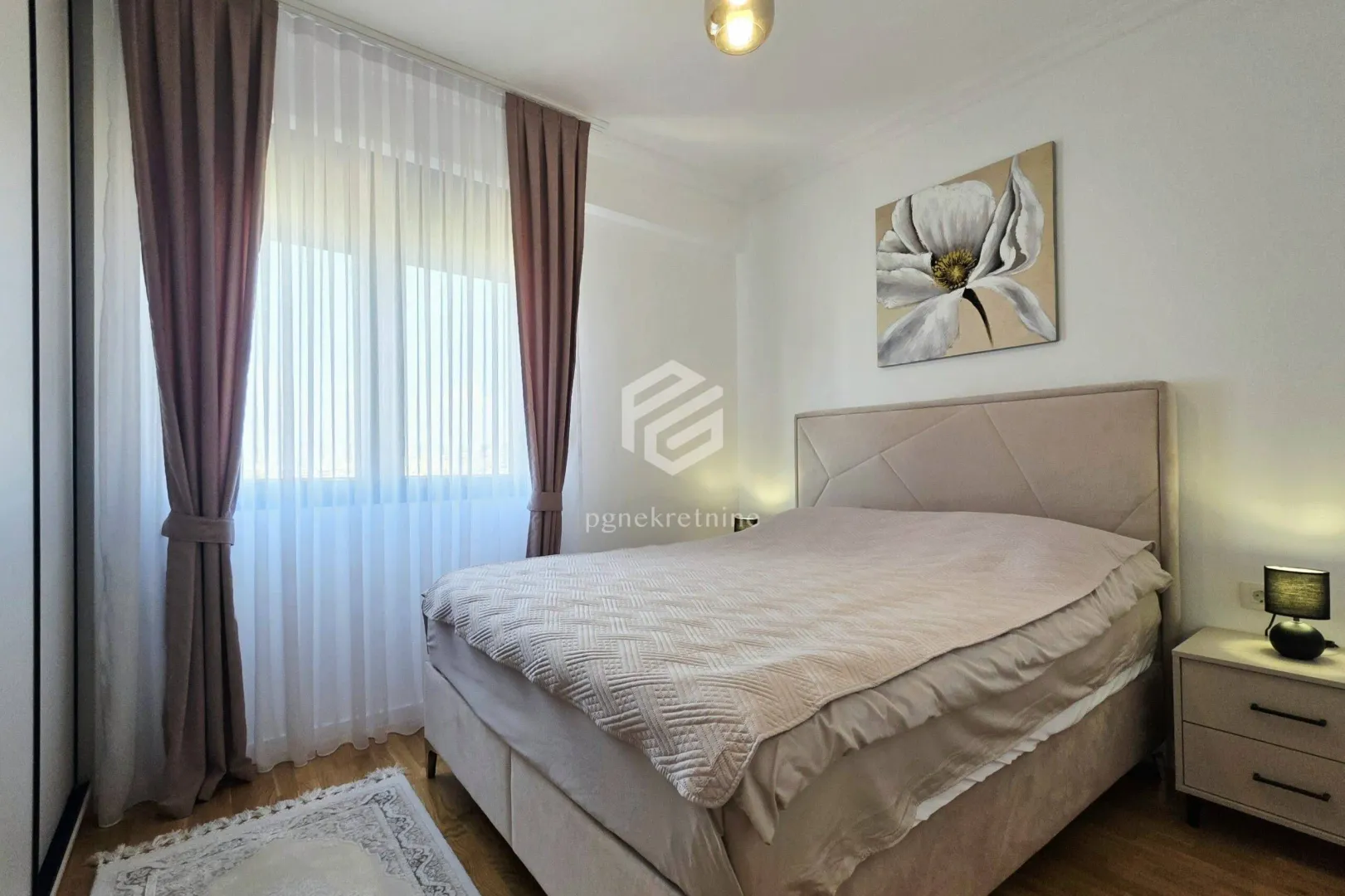 Furnished bedroom with a double bed, nightstand, and a window with curtains.