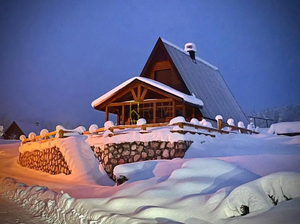 Snimak drvene vikendice pod snijegom tokom sumraka.