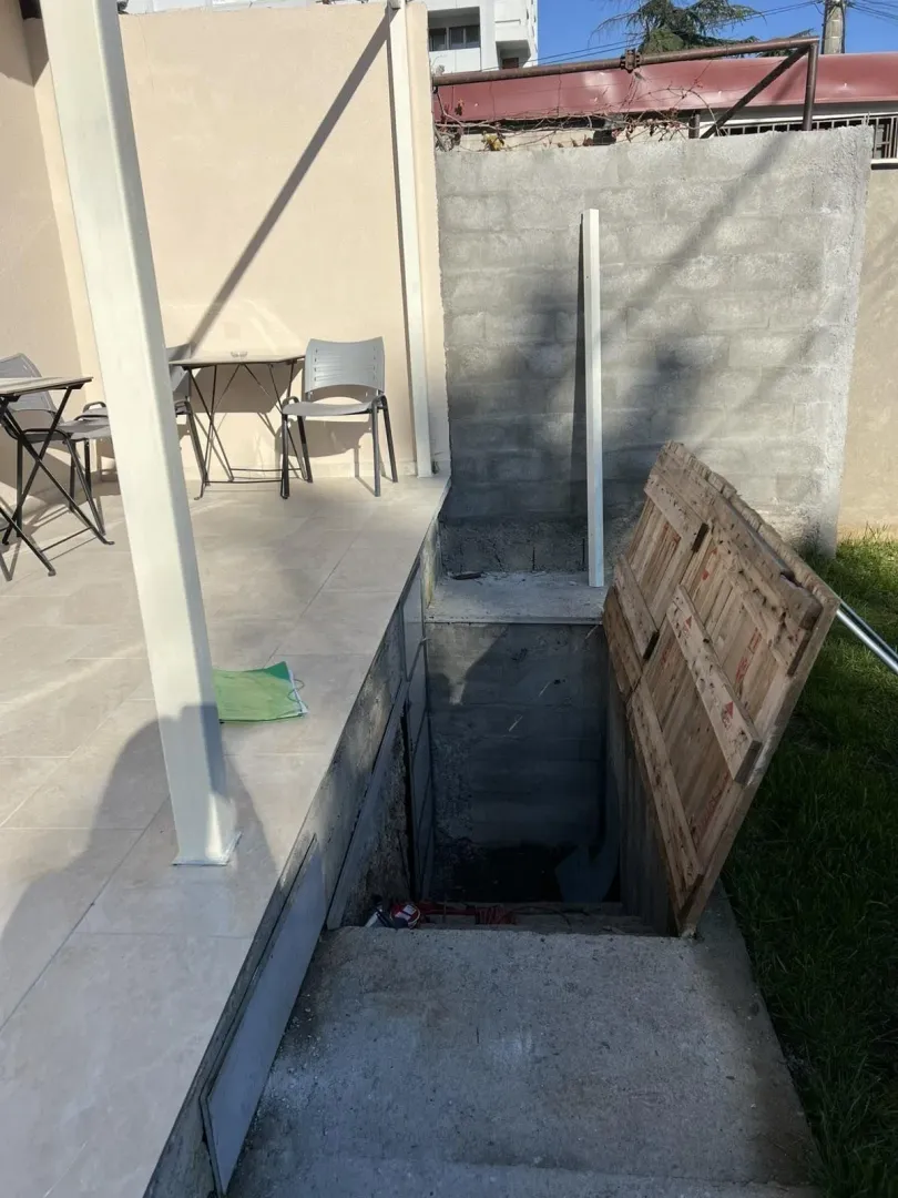 Outdoor area with a tiled terrace and an open entrance to the basement.