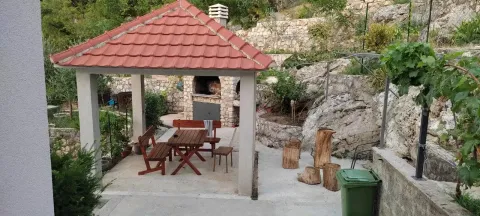 Covered gazebo with a wooden dining set and stone barbecue in the yard. - image 6