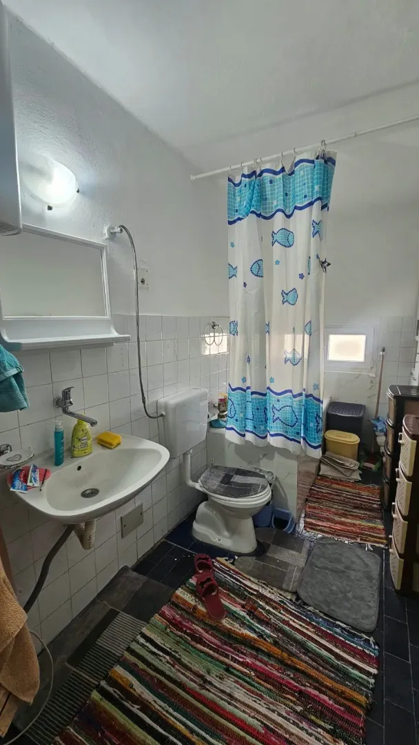 Manje uredno kupatilo sa umivaonikom, wc šoljom i tuš zavjesom.