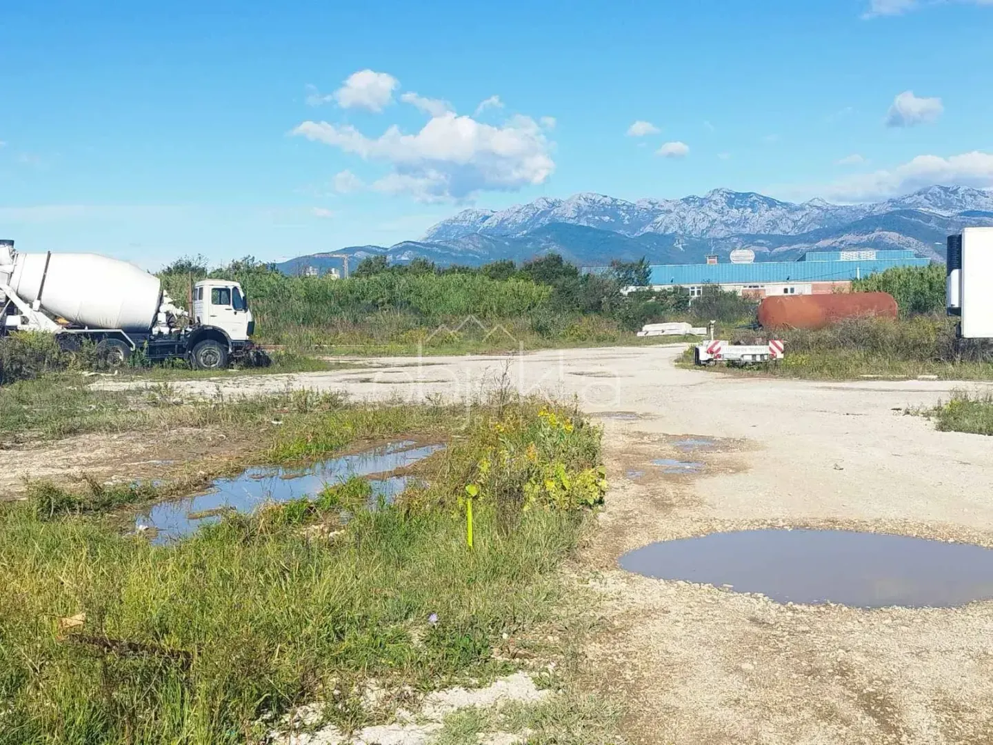 Pogled na plac sa parkiranim kamionom i planinama u pozadini.