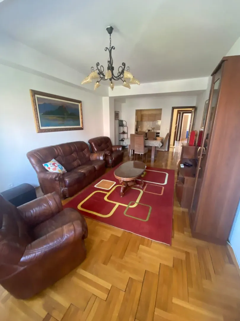 Prostrani dnevni boravak sa garniturom od kože, trpezarijom u pozadini i drvenim podom.