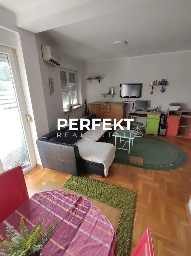 Dnevna soba sa garniturom, radnim stolom i trpezarijskim stolom u prvom planu.