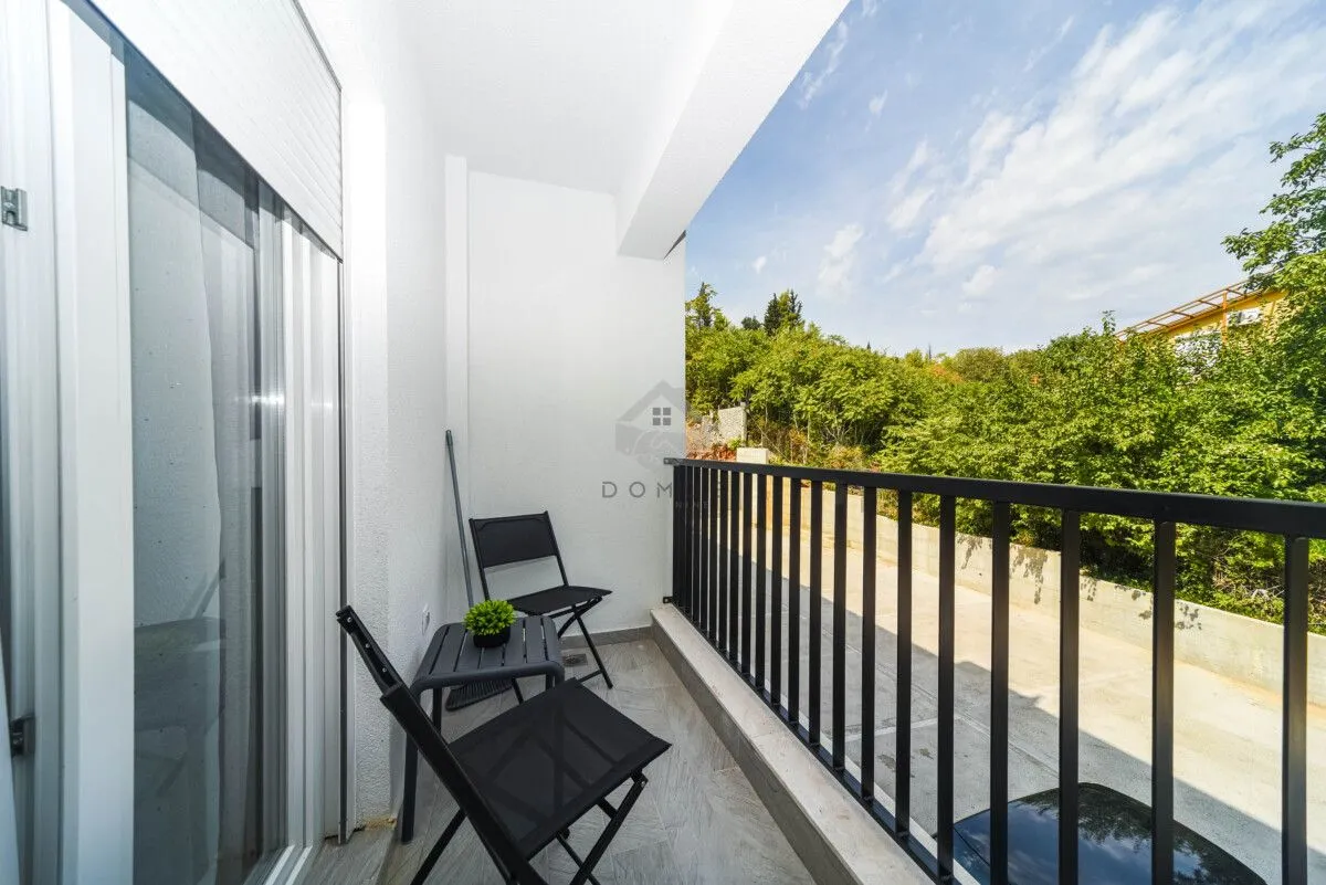 Manji svijetli balkon sa crnim stolom i stolicama i pogledom na zelenilo.