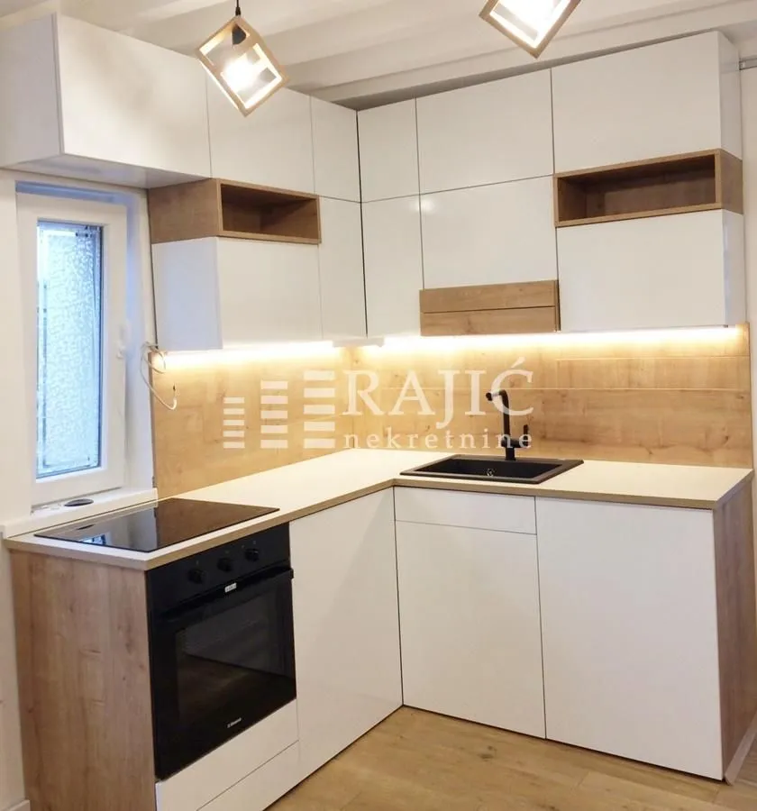 Modern white kitchen with wooden accents and built-in oven.