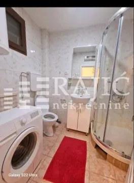 Smaller bathroom equipped with a shower cabin, sink, toilet, and washing machine. - image 8