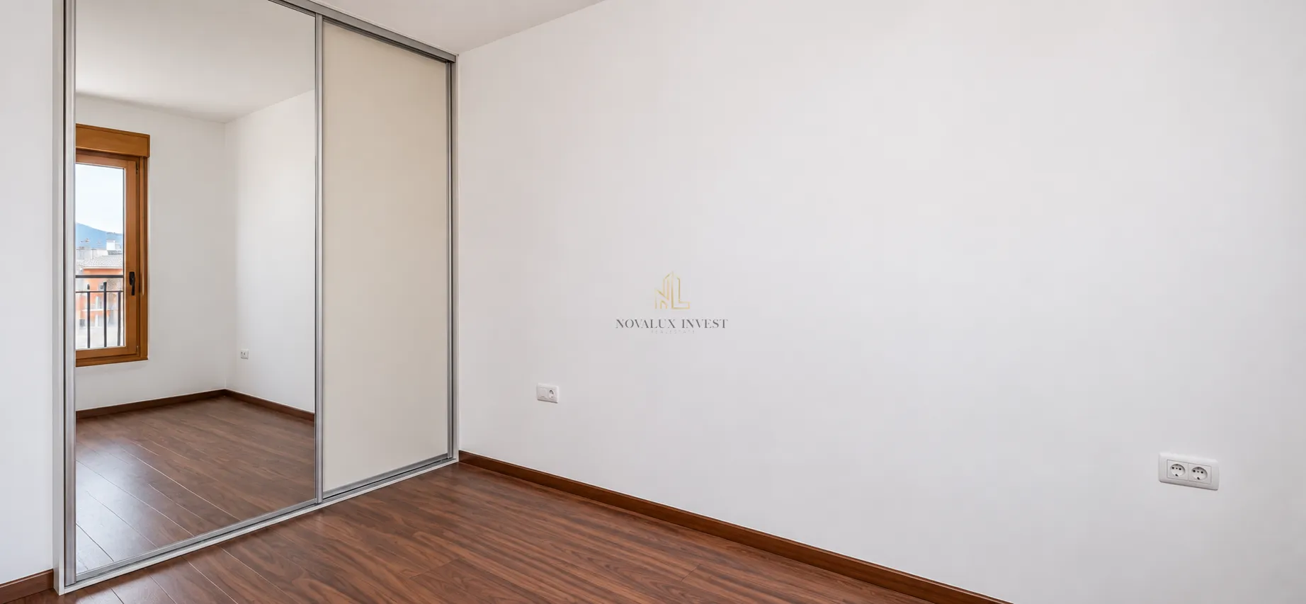 Empty room with a built-in mirrored wardrobe and hardwood flooring.