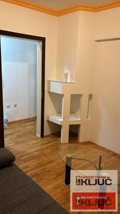 Dnevna soba sa garniturom, staklenim stočićem i ugradnim policama na zidu.