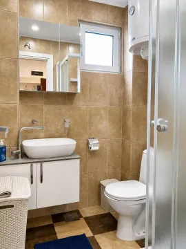 Kompaktno kupatilo obloženo braon pločicama sa umivaonikom i WC šoljom. - image 2