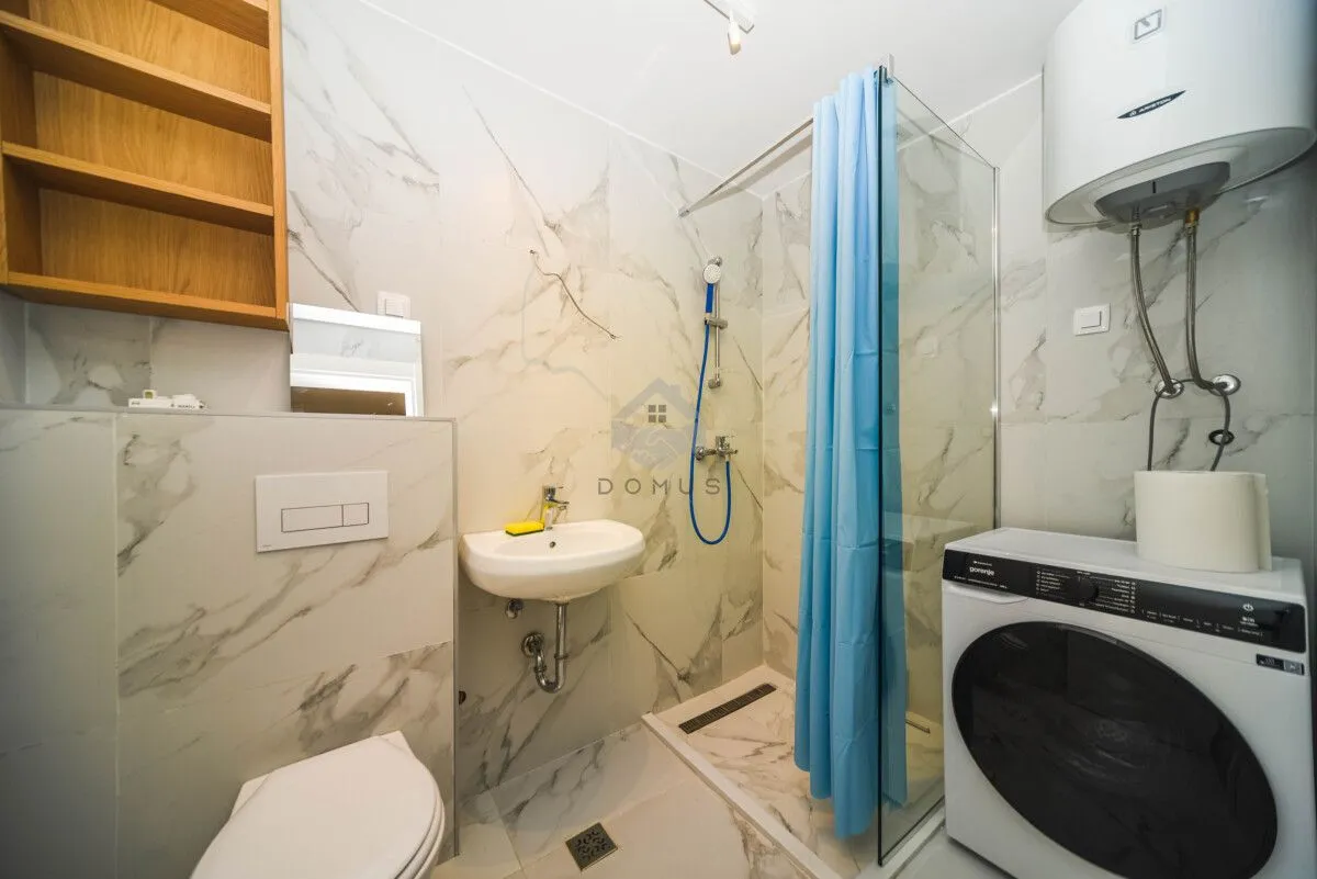 Bathroom with a shower cabin, washbasin, toilet, and washing machine.