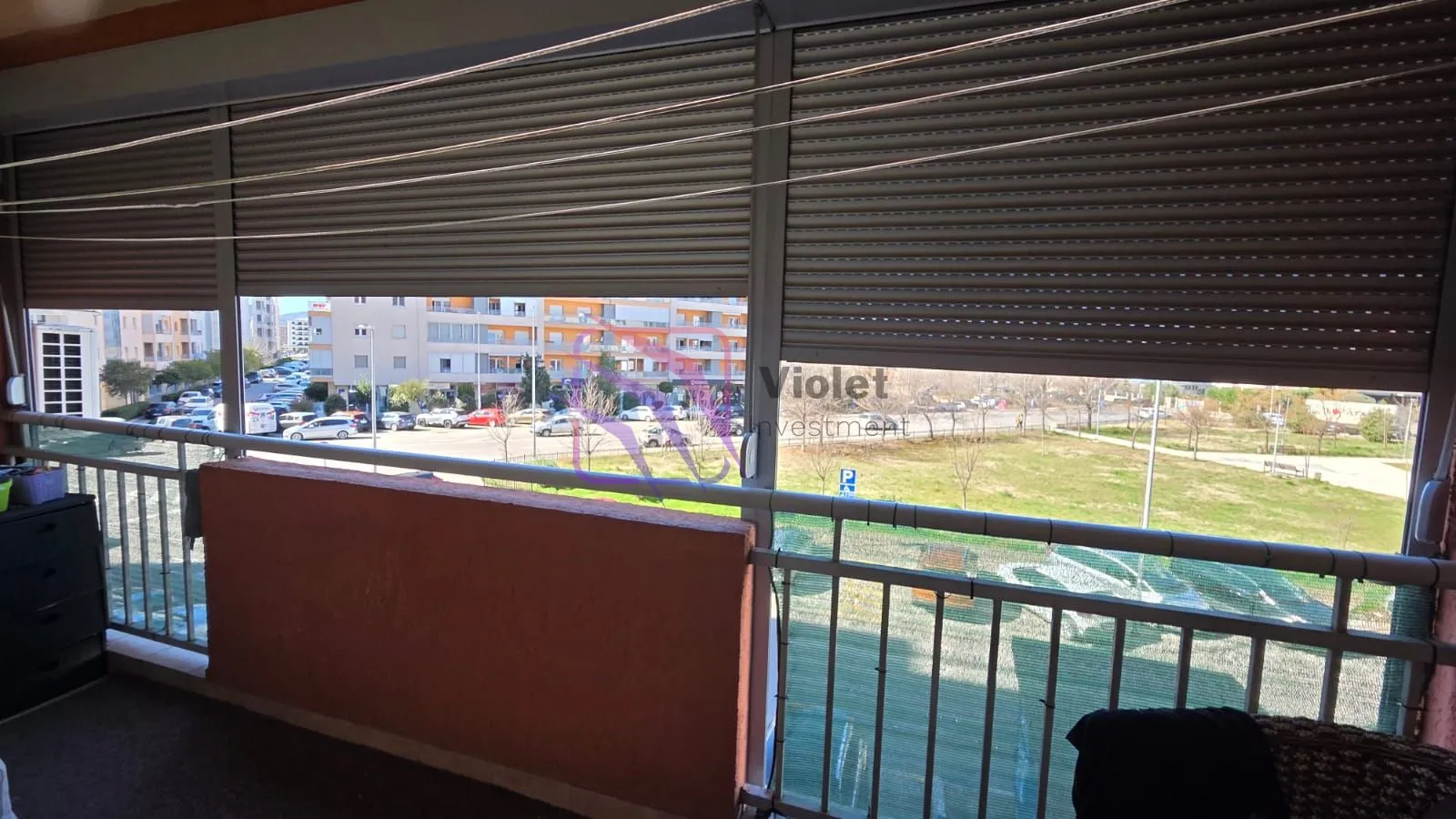 Natkriveni balkon sa spuštenim roletnama i pogledom na ulicu i parking.