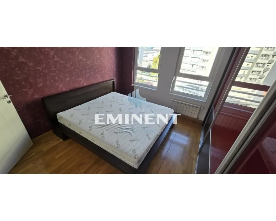 Furnished bedroom with a double bed and windows overlooking surrounding buildings.