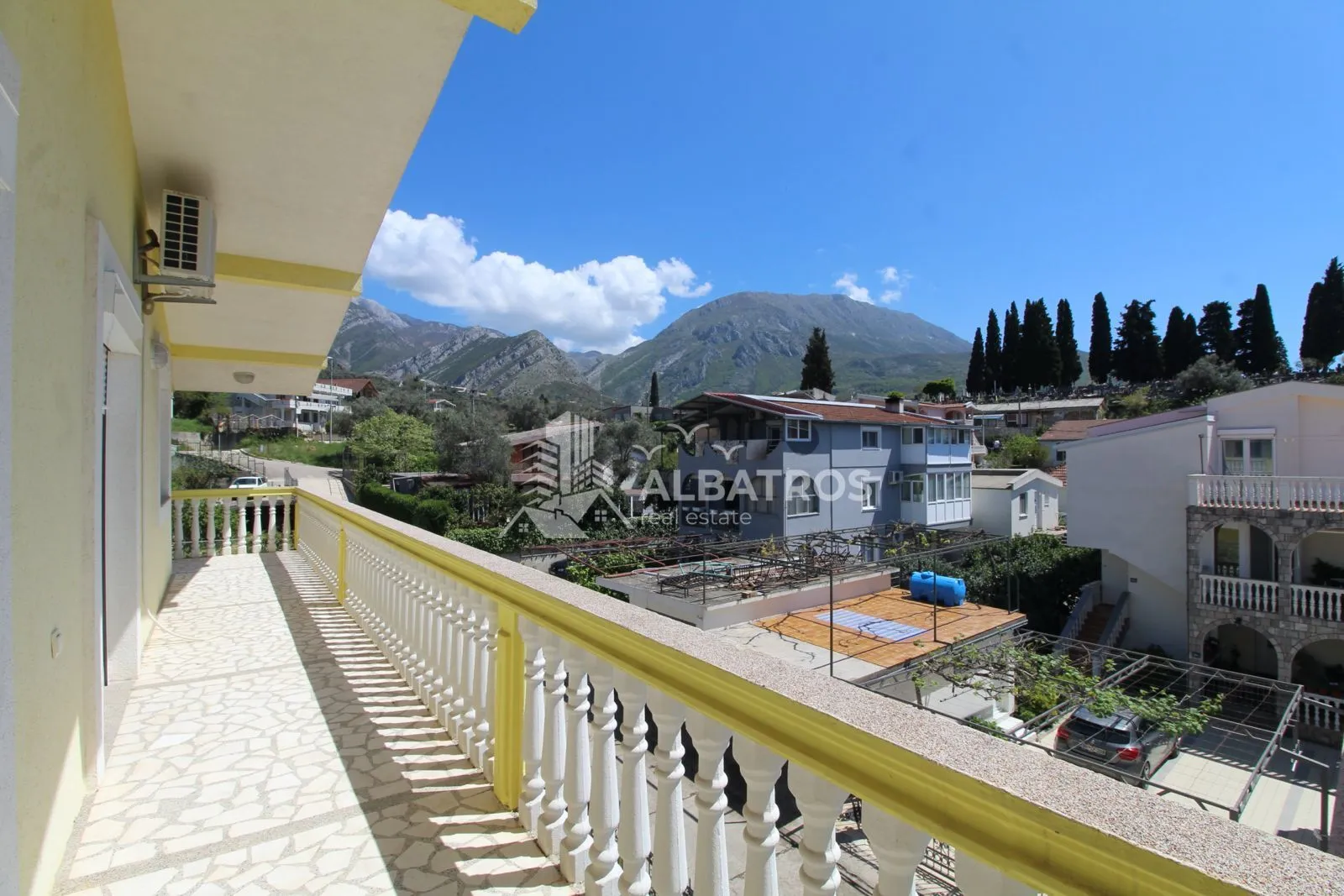 Dugačak balkon sa pogledom na naselje i okolne planine.