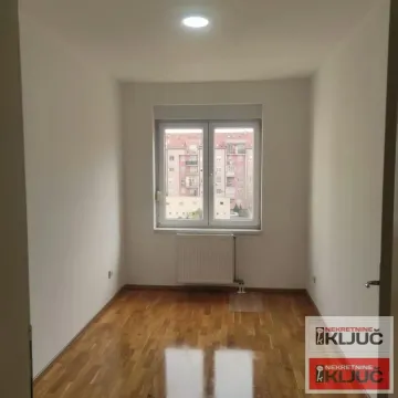 Prazna soba sa parketom i prozorom koji gleda na susedne zgrade. - image 4