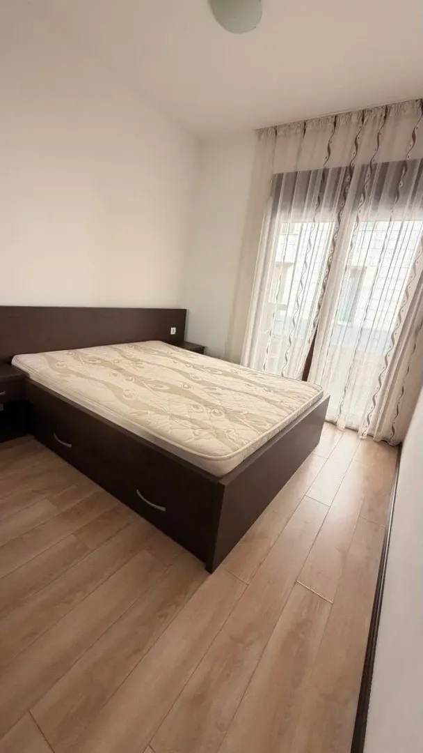 Spavaća soba sa bračnim krevetom i prozorom sa svijetlim zavjesama.