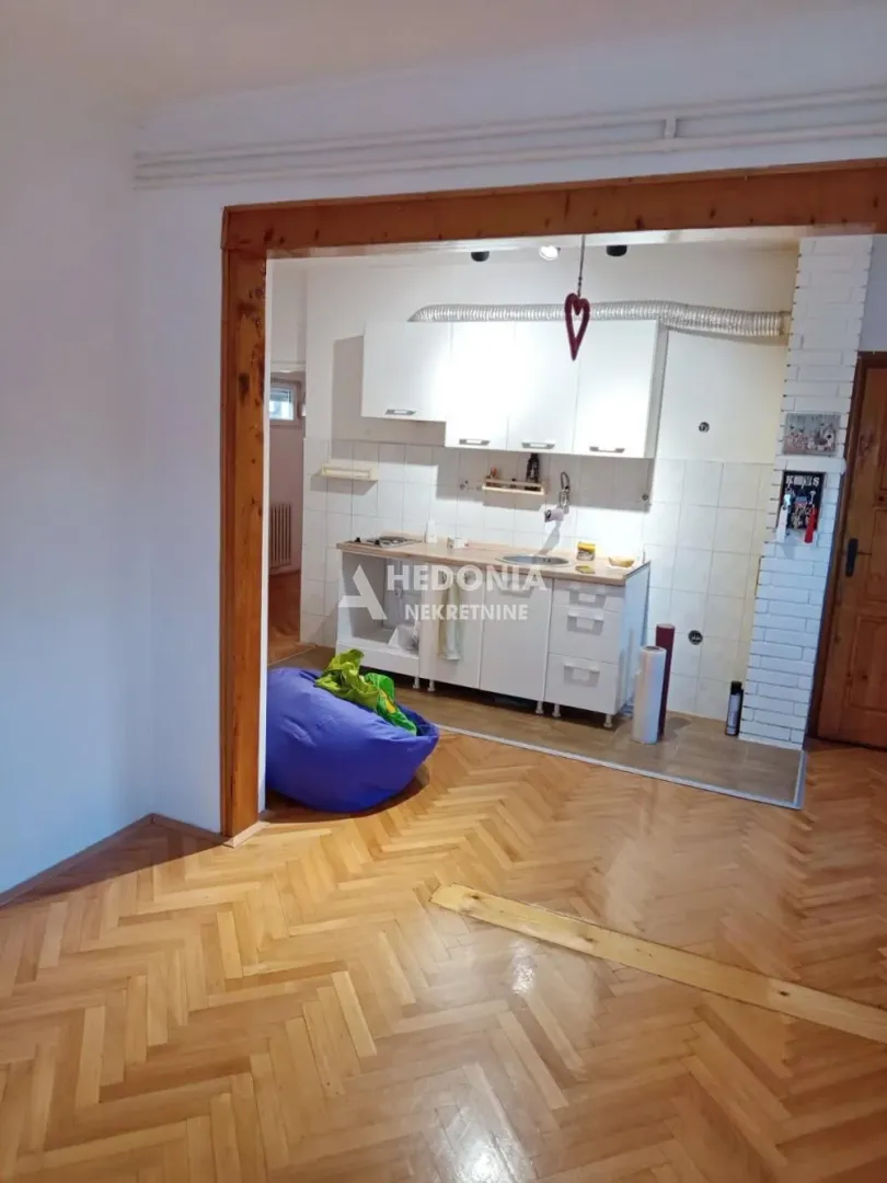 View from the room into a small kitchen with white cabinets and wooden flooring.