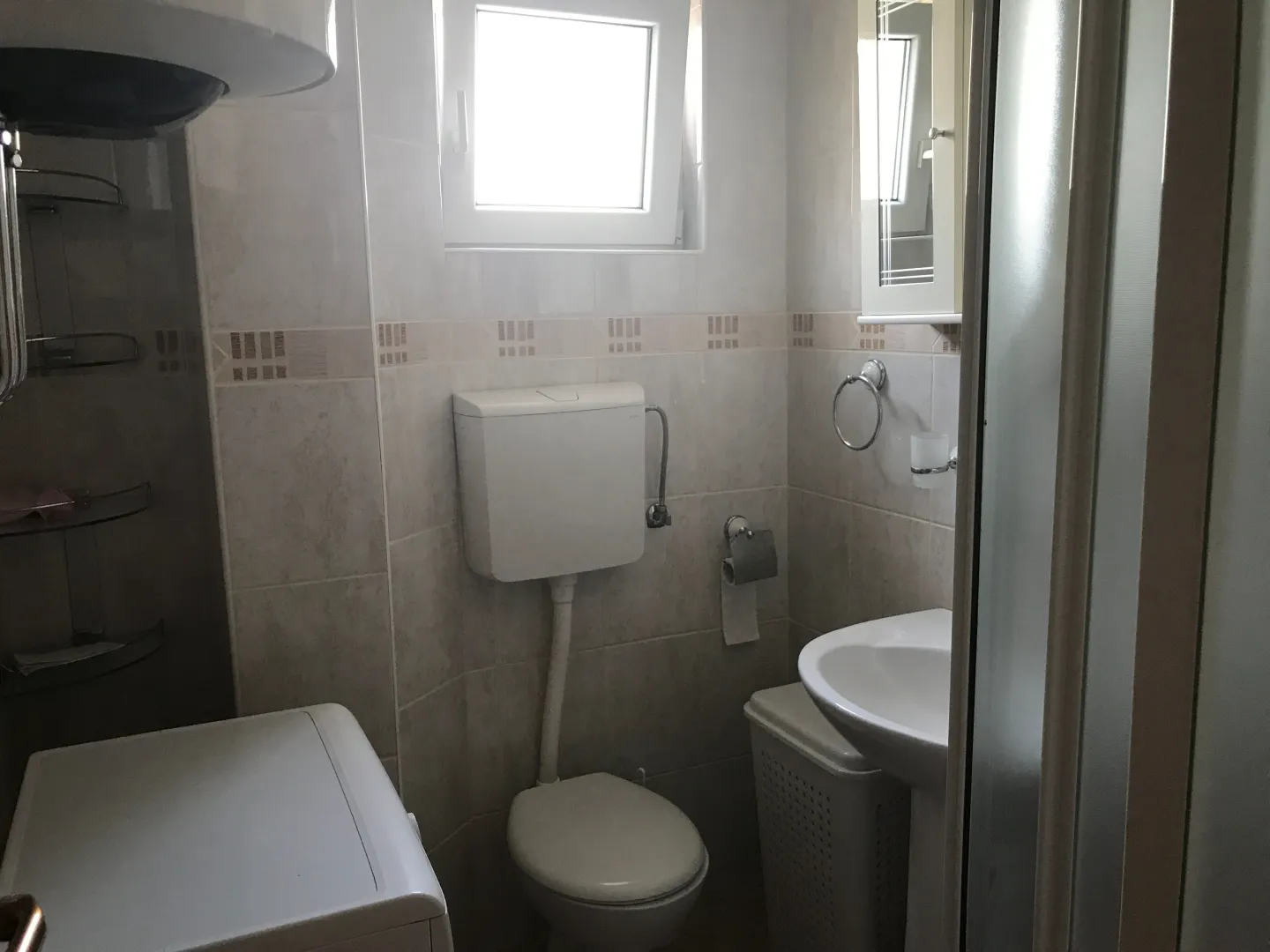 Compact bathroom with a sink, toilet, shower cabin, and washing machine.