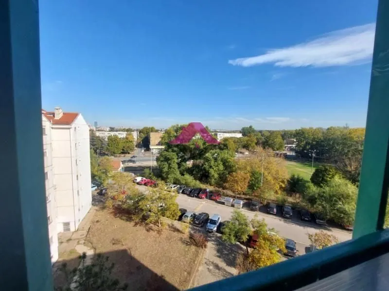 Pogled sa prozora na okolne zgrade, parking i zelenilo.