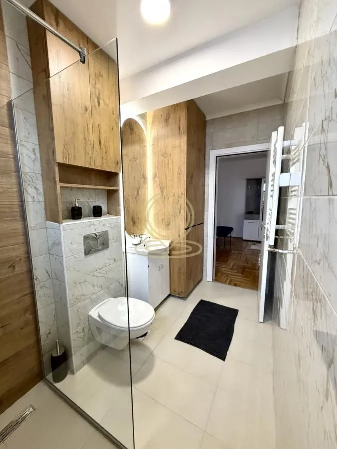 Modern bathroom with a walk-in shower, wall-hung toilet, and wooden cabinetry.