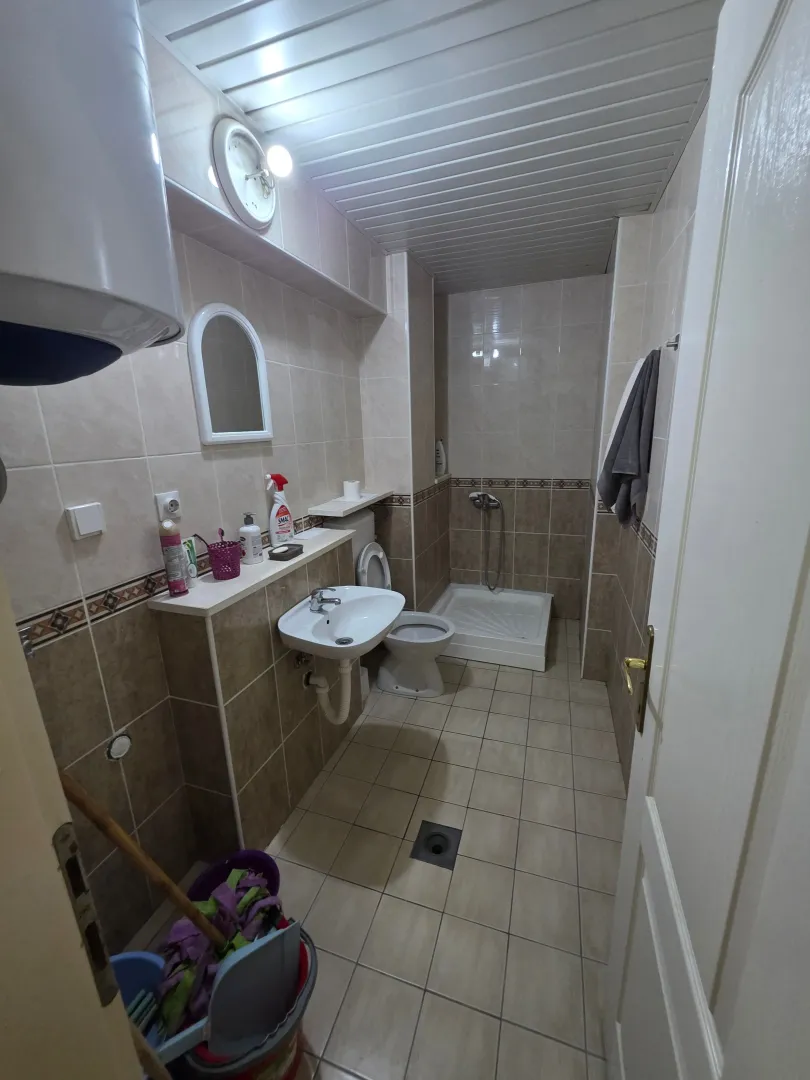 Manje kupatilo sa tuš kabinom, umivaonikom i WC šoljom u bež pločicama.