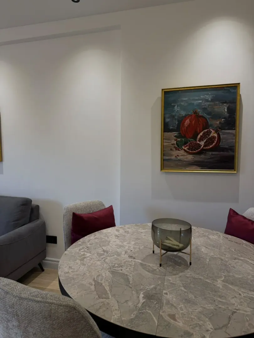Dining area with a round table and chairs, decorated with an artwork on the wall.