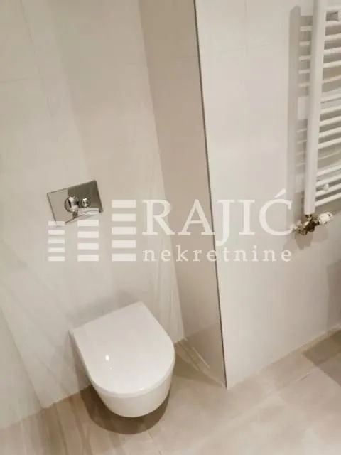 View of a modern bathroom with a wall-hung toilet and a towel radiator.