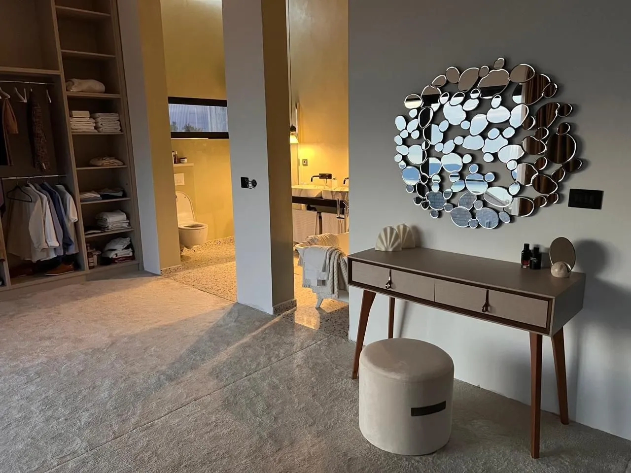 Modern bedroom with a walk-in wardrobe, vanity table, and a view of the bathroom.