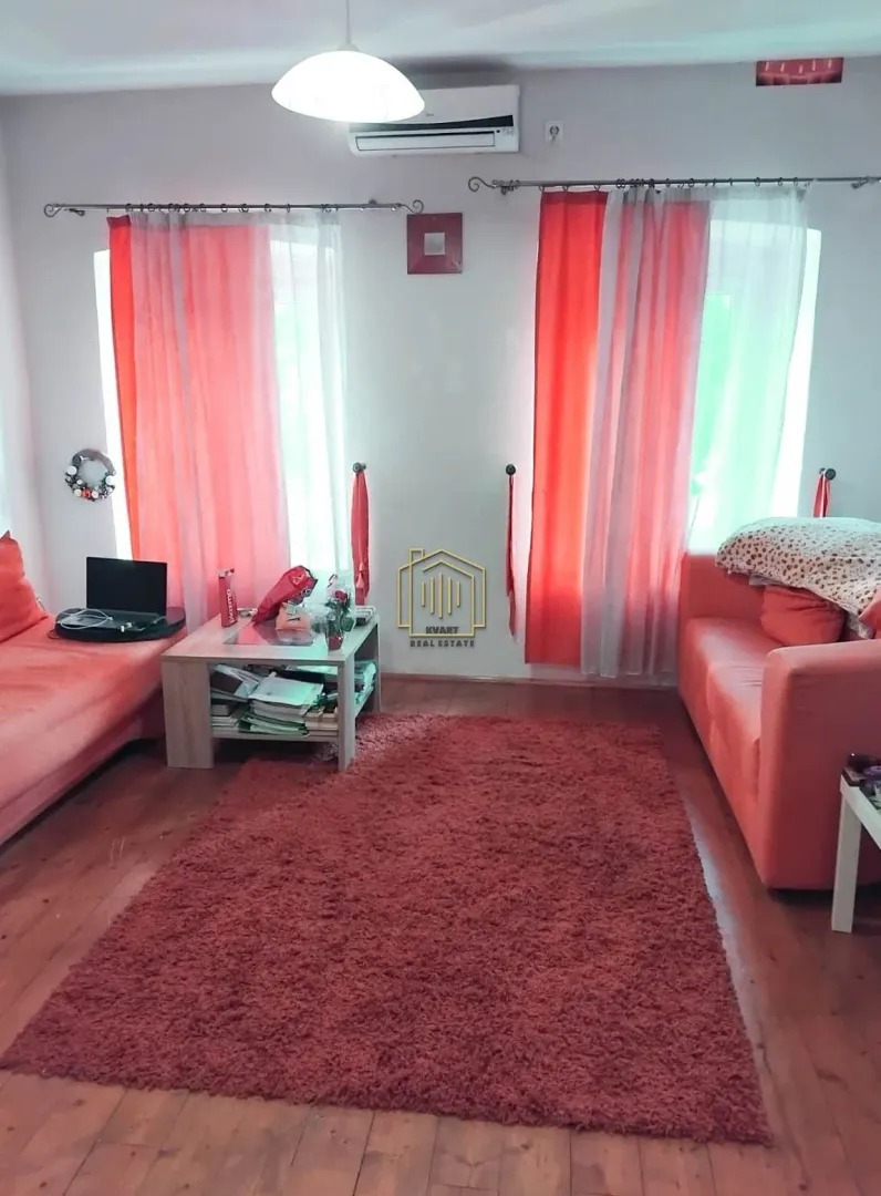 Dnevna soba sa sofama, stočićem i crvenim tepihom.
