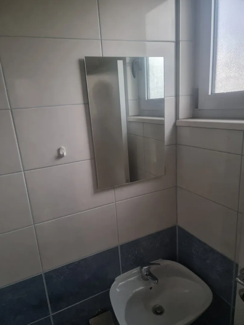 Manje kupatilo sa umivaonikom, ogledalom i pločicama na zidovima.