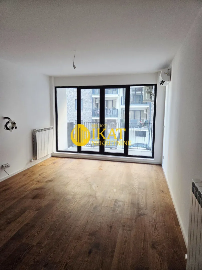 Empty room with wooden flooring, white walls, and large glass doors leading to a balcony.