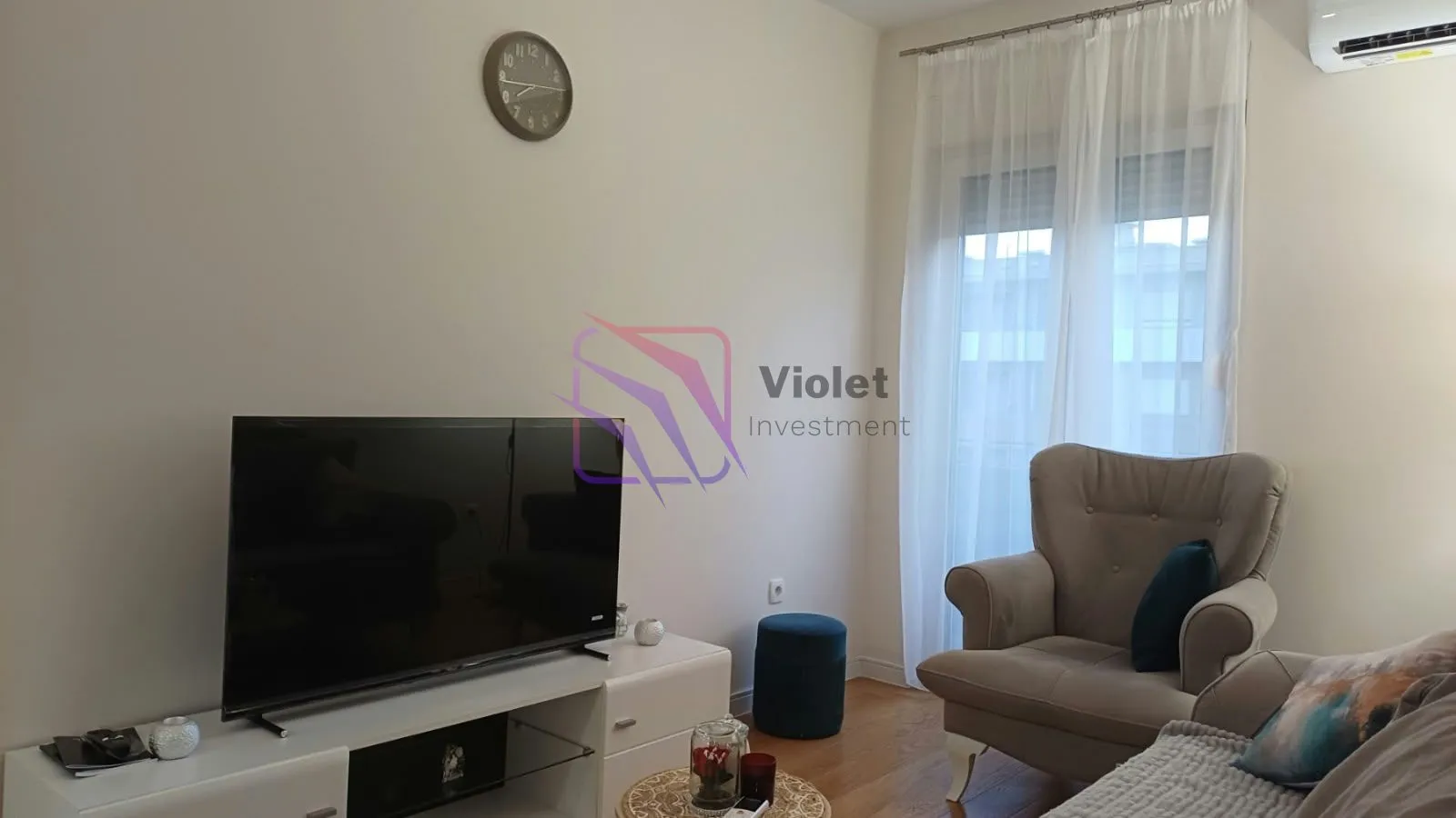 Living room with a TV, armchair, and balcony access.