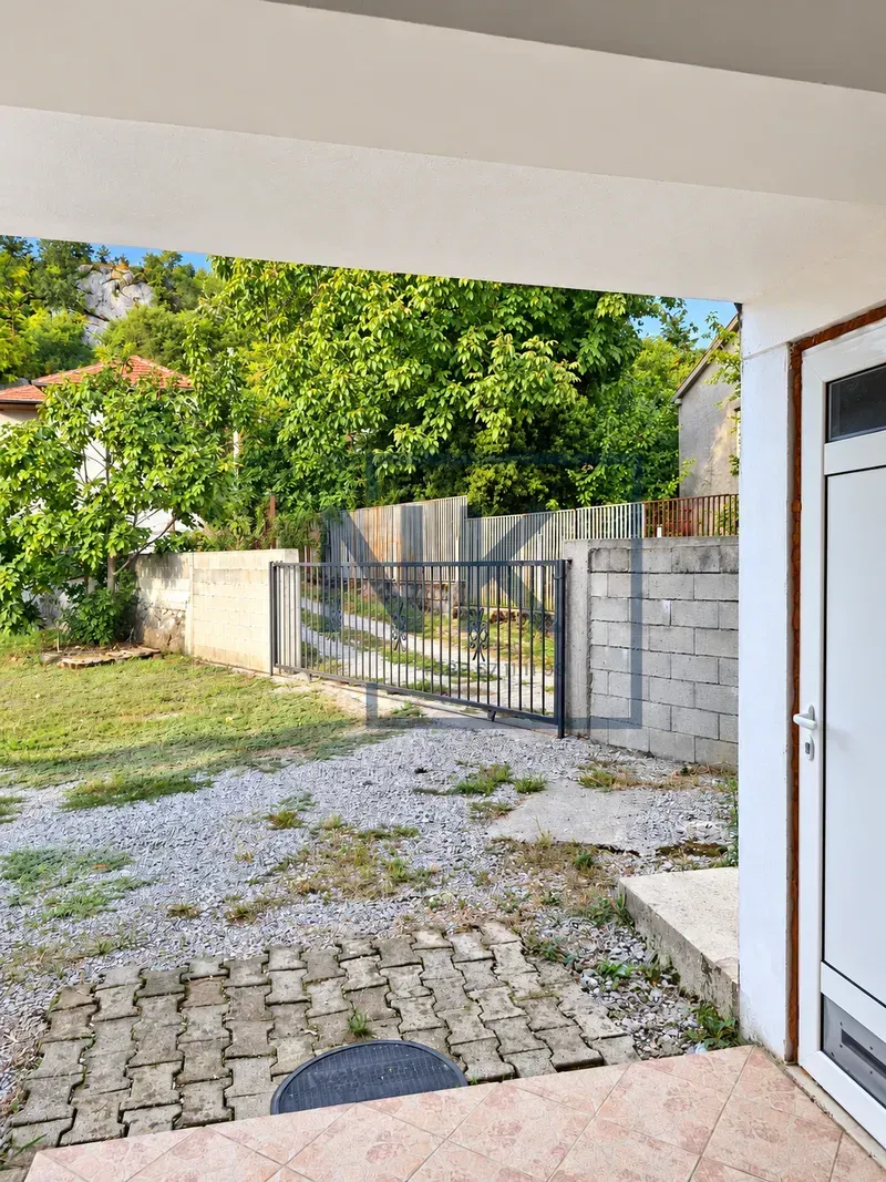 View from the covered porch toward the yard with a fence and greenery.