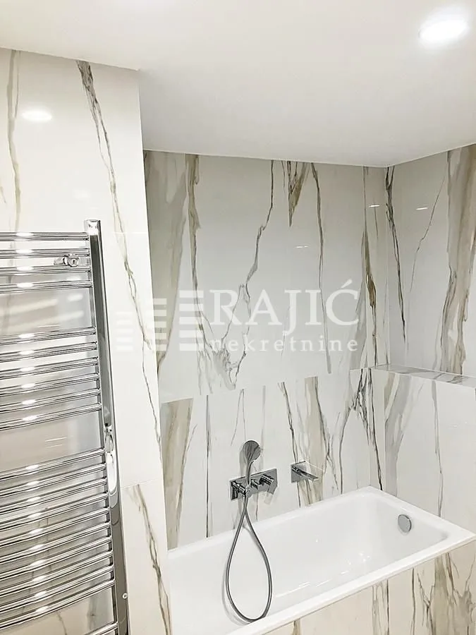 Modern bathroom with white marble-pattern tiles, bathtub, and a chrome towel warmer.
