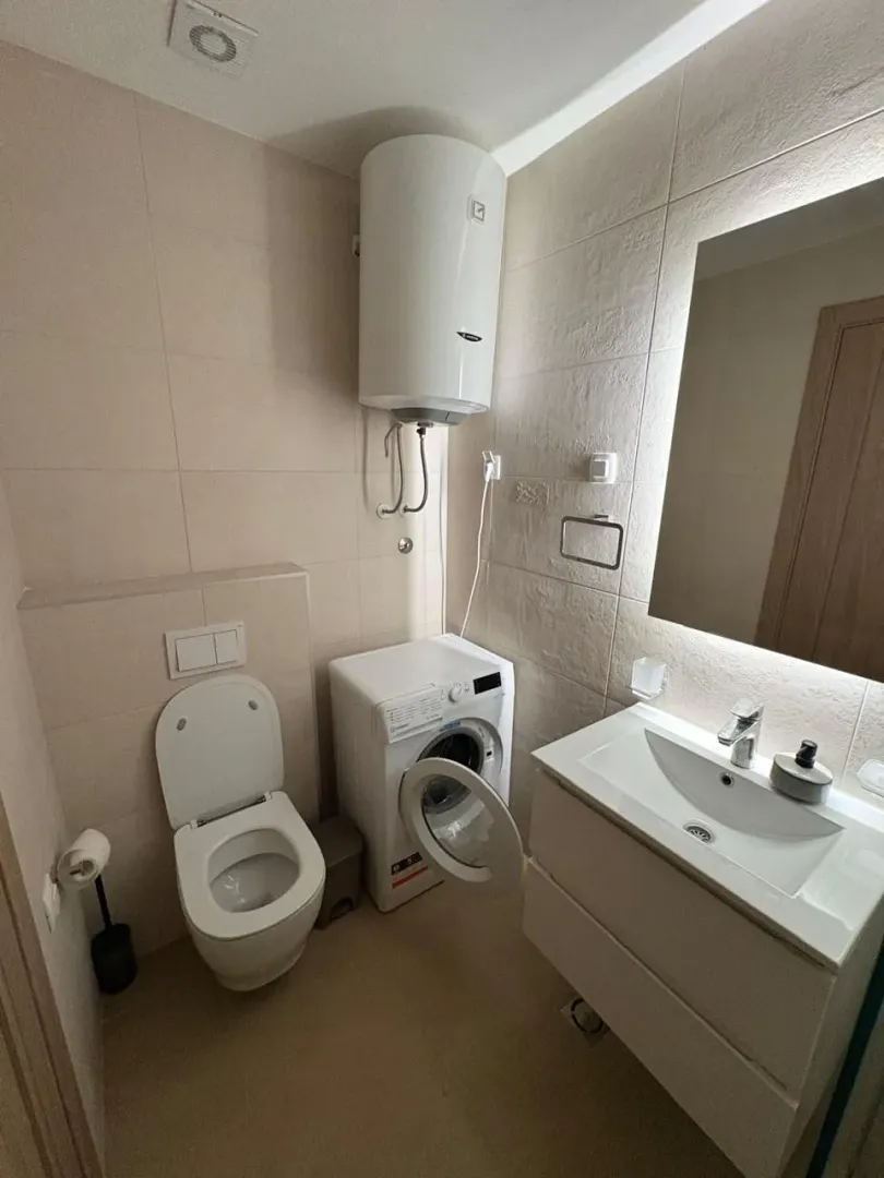 A neatly equipped bathroom with a sink, toilet, water heater, and washing machine.