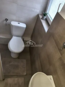 Manje kupatilo sa WC šoljom, lavaboom i keramičkim pločicama u braon tonovima. - image 3