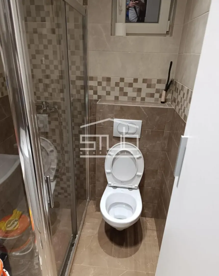 Manje kupatilo sa tuš kabinom i WC šoljom u popločanom prostoru.